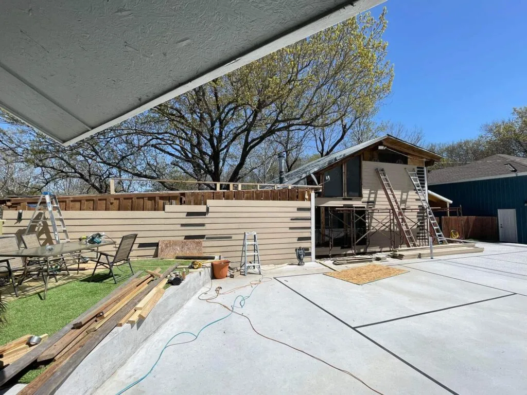Exterior siding replacement in progress with ladders and scaffolding.